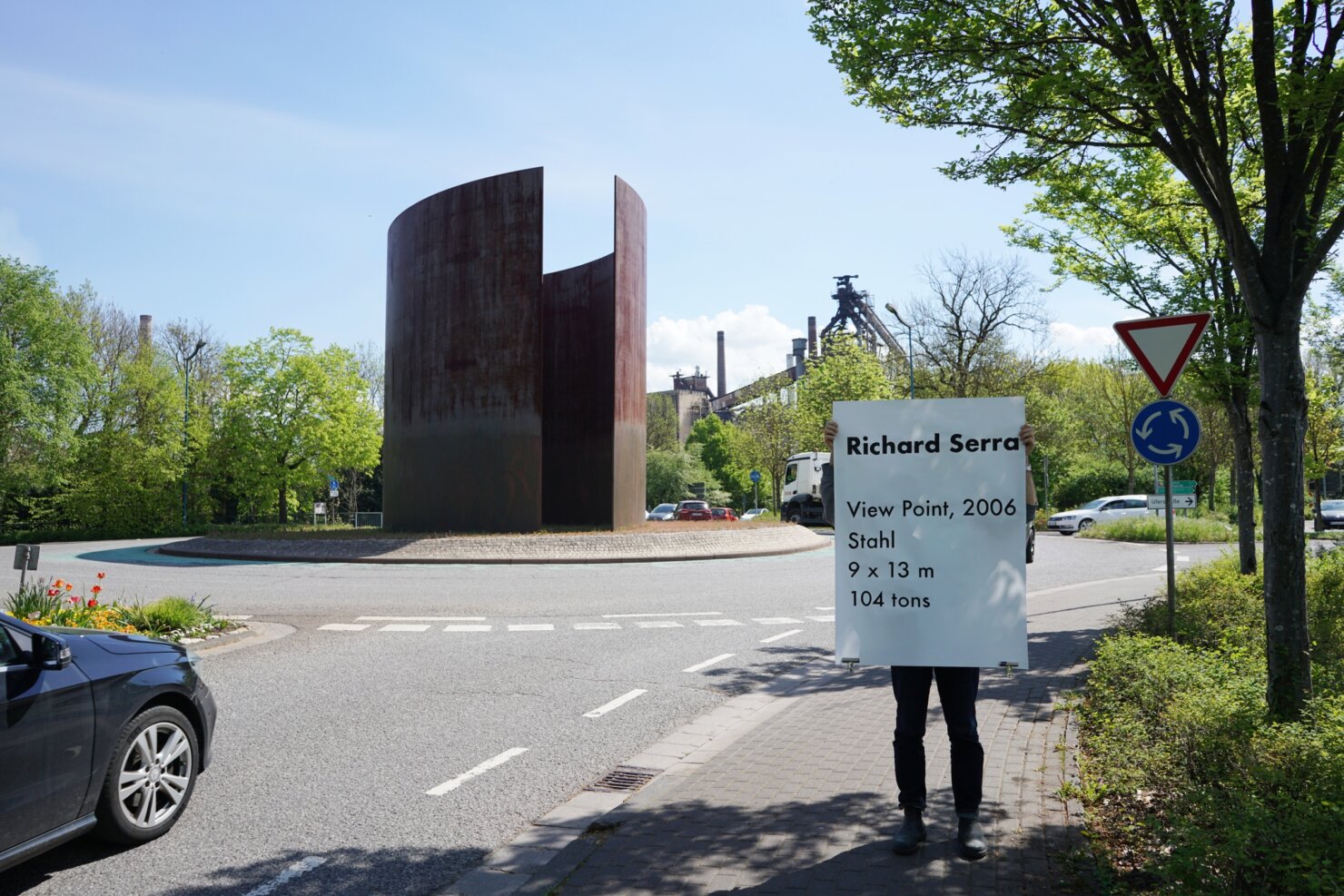 Matthieu Martin, Kreisverkehr, performance with monumental label near public sculpture, Dillingen, 2026